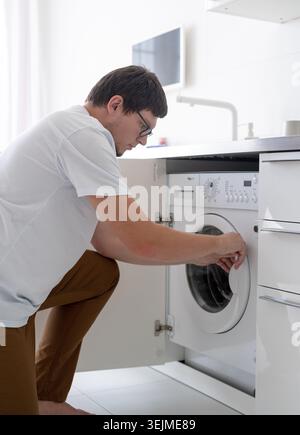 Giovane uomo che mette i vestiti in lavatrice Foto Stock