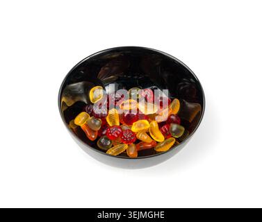 Caramelle gommose di frutta in una ciotola nera isolata, pillole vegane di marmellata da masticare, mucche di gelatina, caramelle colorate su sfondo bianco Foto Stock
