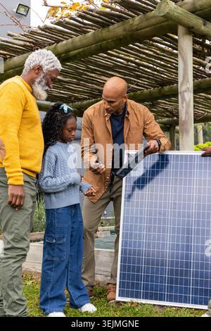 Famiglia afroamericana, anziani e bambini che ispezionano il pannello solare sotto il pergolato, uomo che tiene il metro. Giardino, cortile, rustico, foto Foto Stock