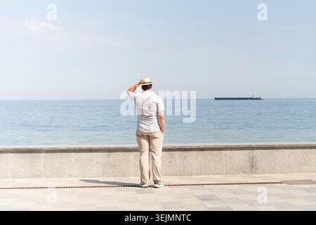 Giovane uomo in abiti estivi in piedi su un molo, mare sullo sfondo Foto Stock