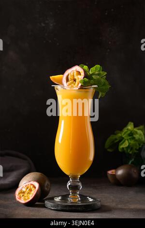 Cocktail al frutto della passione e al mango o succo di frutta in bicchiere di uragano su nero. Foto Stock