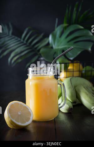 Succo di frutta fresco estivo con banana, limone al buio. Foto Stock