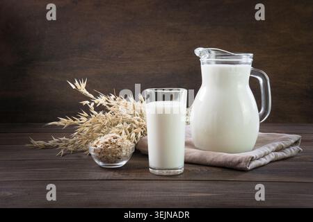 Latte d'avena fresco in vetro e caraffa su un tavolo di legno scuro. Stile rustico. Foto Stock