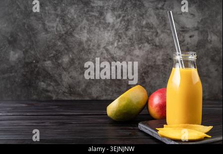 Frullato di mango fresco in un bicchiere con cannuccia metallica decorata con fette di mango vista frontale su sfondo di legno scuro Foto Stock