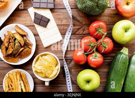 Concetto di cibo sano e malsano. Frutta e verdura, dolci e patatine fritte, vista dall'alto su sfondo in legno Foto Stock