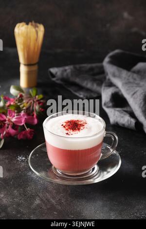 Latte matcha rosa con fiori sakura decorati a polvere su sfondo nero. Foto Stock
