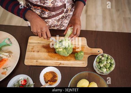 Donna che taglia i broccoli su una tavola di legno per una sana preparazione dei pasti Foto Stock