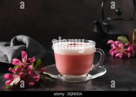 Latte matcha rosa con fiori sakura decorati a polvere su sfondo nero. Foto Stock
