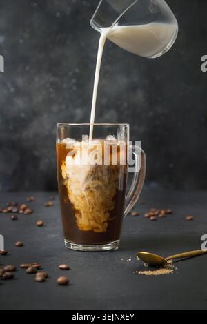 Caffè a latte freddo in bicchiere da tazza con latte versato sul nero Foto Stock