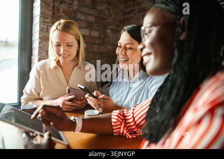 Amici diversi che amano la tecnologia e sorridono al bar Foto Stock