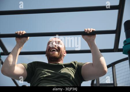Il bel barbuto fa i tiri sul bar orizzontale in strada sul campo sportivo. Foto Stock