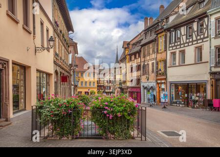 Vista di una strada storica a Colmar in Alsazia Francia con decorazioni floreali. Architettura tradizionale sotto un cielo parzialmente nuvoloso Foto Stock