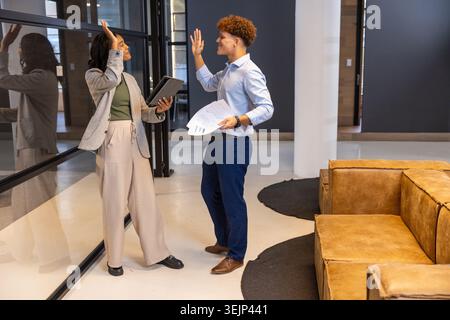 Diversi colleghi in blazer molto vivaci in sala corridoio d'ufficio con tablet e pagine stampate. Professionale, lavoro di squadra, mod Foto Stock