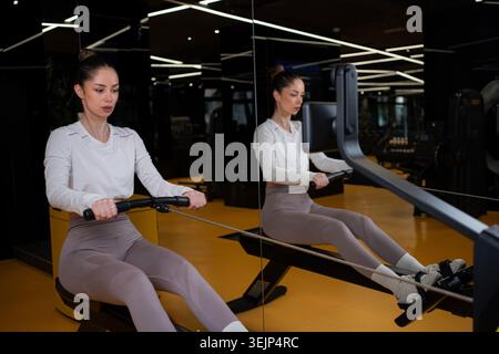 Donna che si allena con una macchina per remare in palestra Foto Stock
