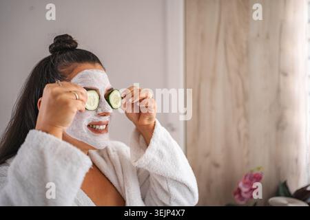 Donna sorridente che indossa un accappatoio e si sottopone a un trattamento di bellezza a casa Foto Stock