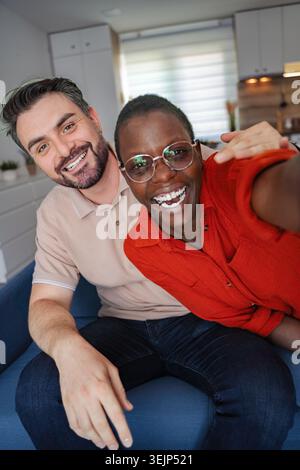 Coppia interrazziale che fa un selfie sul divano, sorride e ride Foto Stock