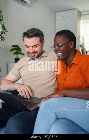 Coppia che si rilassa sul divano, naviga su Internet con un computer portatile e sorride Foto Stock