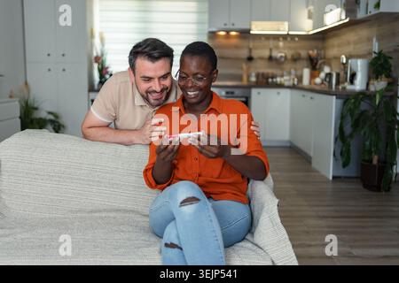 Felice coppia interrazziale che guarda il risultato positivo del test di gravidanza Foto Stock