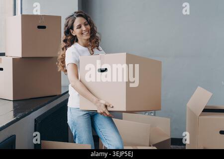 Trasferirsi in una nuova casa. Felice locatario donna che trasporta una scatola di cartone con oggetti per il trasferimento Foto Stock