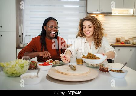 Diverse donne e amici che si divertono a cucinare pasti sani insieme in cucina Foto Stock