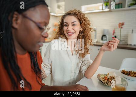 Diverse amiche si godono il pranzo e la conversazione in cucina Foto Stock
