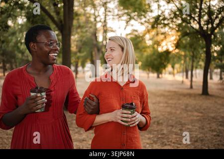 Due diverse donne si godono una conversazione e una bevanda mentre passeggiano in un parco Foto Stock