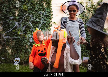 Bambini felici che indossano costumi di Halloween che giocano con la loro babysitter nel cortile Foto Stock
