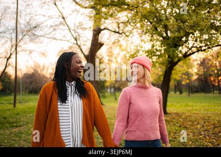 Diverse donne e amici ridono camminando mano nella mano nel parco Foto Stock