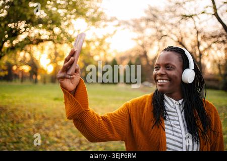 Donna che effettua videochiamate al parco durante il tramonto autunnale Foto Stock