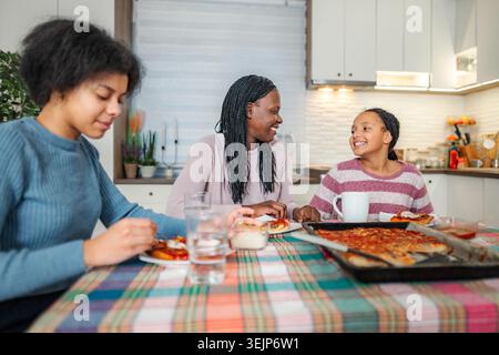 La famiglia si diverte a mangiare la pizza e a parlare a casa Foto Stock