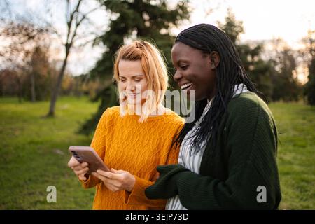 Diverse amiche di sesso femminile che discutono di contenuti su smartphone in parco Foto Stock