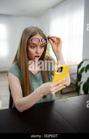 La donna si sorprende mentre usa lo smartphone a casa Foto Stock