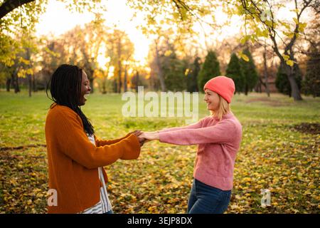 Amici diversi che si tengono per mano ridendo nel parco autunnale Foto Stock