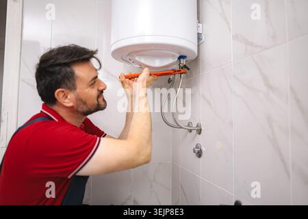 Idraulico che fissa uno scaldabagno in un bagno Foto Stock