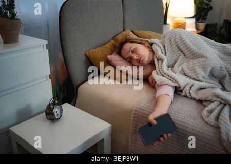Donna che dorme nel letto con smartphone in camera da letto Foto Stock