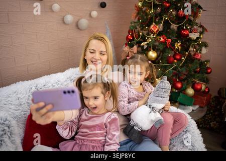 Madre e figlie si fanno selfie sull'albero di natale Foto Stock