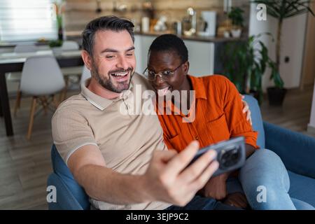 Una coppia giocherellona che porta un selfie sul divano a casa Foto Stock