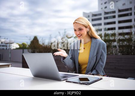 Donna sorridente di videochiamare all'aperto utilizzando un laptop Foto Stock