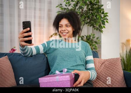 Giovane donna che ha una videochiamata per festeggiare la ricezione di un regalo Foto Stock