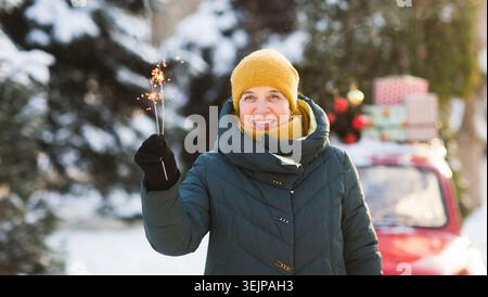 Donna anziana felice in caldi abiti invernali con fuochi d'artificio sparkler in strada. Buon Natale! inverno e vacanze Foto Stock