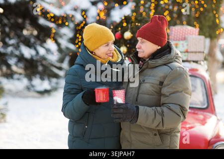 Pensionati di coppia senior con abiti invernali caldi in piedi per strada con tazze di tè. Buon Natale! Foto Stock
