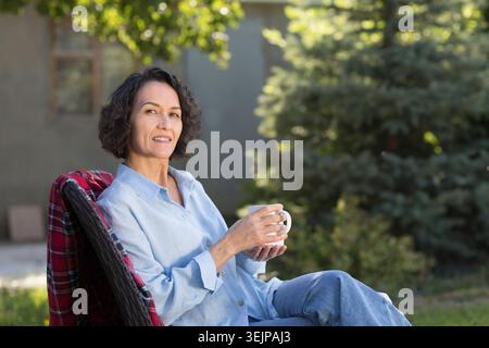 Ritratto di una donna allegra di mezza età con una tazza di tè in giardino intorno alla sua casa in estate. concetto senza stress. uomini Foto Stock