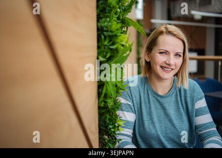 Donna bionda sorridente in un moderno giardino verticale di uffici Foto Stock