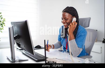 Consulenza infermiera afroamericana al telefono sorridente alla scrivania Foto Stock