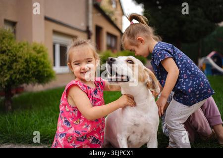 Momenti di gioia condivisi da due bambini con il loro cane giocoso all'aperto Foto Stock