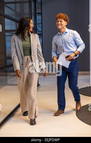 Diversi colleghi che passano davanti alla partizione in vetro nel corridoio dell'ufficio, tenendo in mano documenti e smartphone. Professionale, collaborazione, m Foto Stock