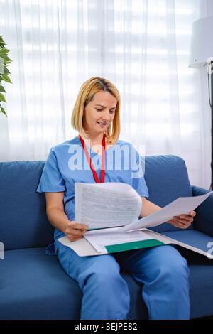 Medico donna che esamina i record medici a casa Foto Stock