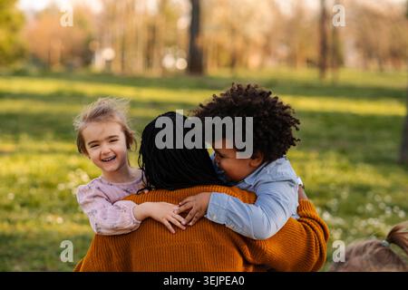 Madre che abbraccia bambini felici in un parco Foto Stock