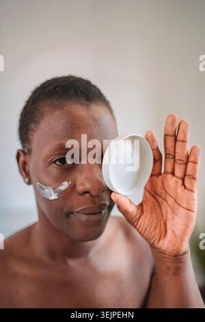 Giovane donna che applica crema idratante sul viso Foto Stock