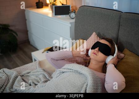Donna che indossa la maschera del sonno e le cuffie che ascolta musica rilassante Foto Stock